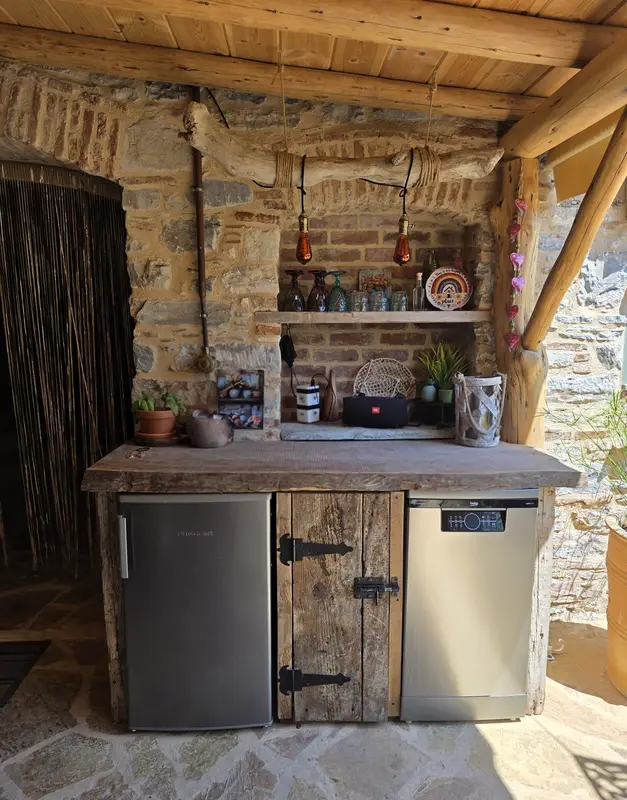 Outdoor kitchen with copper pendant lights, fridge and dishwasher in old wood