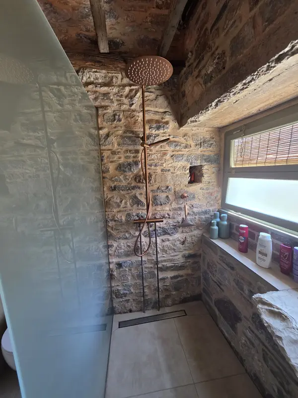 Walk-in shower with a copper rain head against the stone