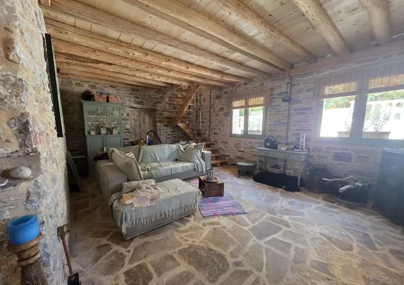 Living room with a beamed ceiling, stone walls and a wooden staircase